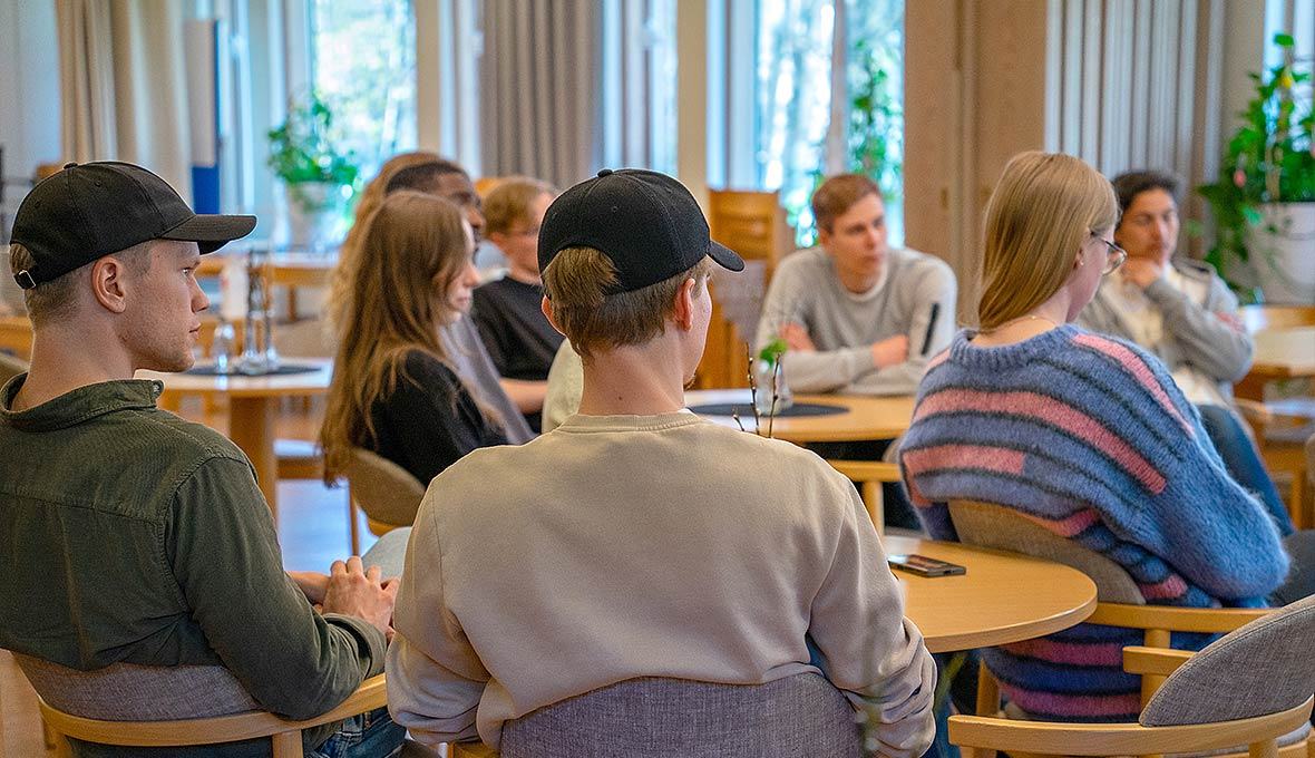Unga vuxna sitter i en ring av stolar och samtalar i en ljus kyrksal.